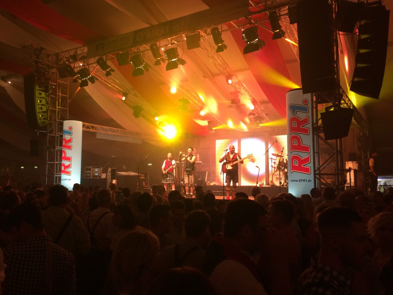 Das Bild zeigt eine Bühne mit einer Band darauf und rechts und links jeweils ein RPR1. Jack in the Box. Vor der Bühne erkennt man eine Menschenmenge.