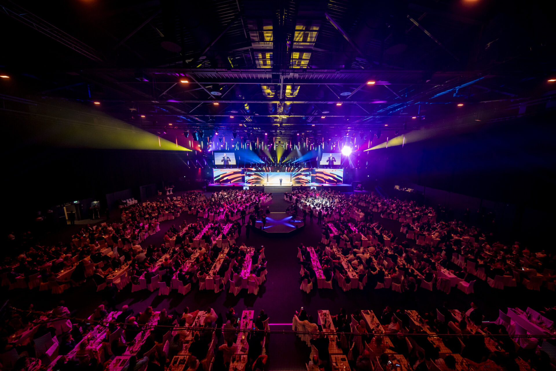 Blick auf die Bühne beim Radio Regenbogen Award mit Tischen und geladenen Gästen. Moderator steht auf der Bühne.