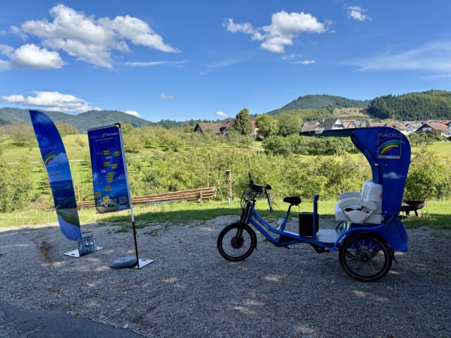 Fahrradrikscha im RADIO-REGENBOGEN-Look auf einer Straße im Grünen