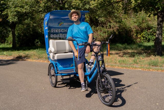Mann mit blauer Kleidung und Helm auf einer Fahrradrikscha